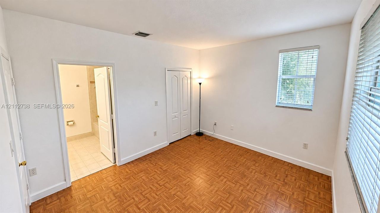 Room featuring parquet wood flooring, neutral wall tones, bi-fold closet doors, and multi-pane windows with horizontal blinds