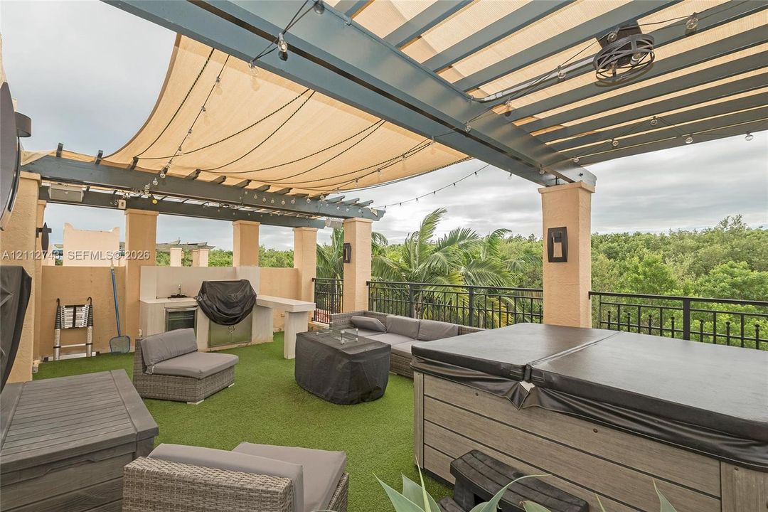 Rooftop terrace featuring a covered pergola with a retractable shade canopy, built-in outdoor kitchen, integrated lighting, and a composite-finish hot tub