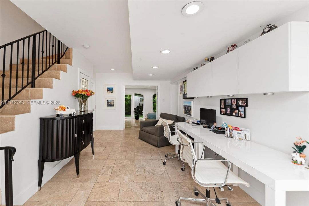 Stone-tiled flooring, built-in white desk with overhead cabinetry, and staircase featuring a black metal railing