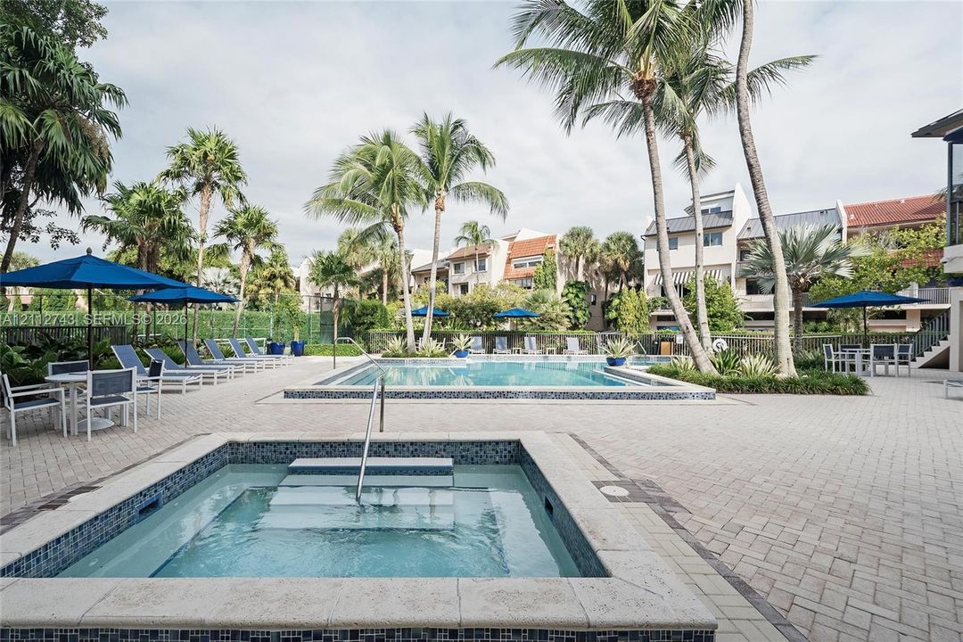 Outdoor swimming pool and spa featuring a stone-paver deck, built-in steps, and surrounding palm trees