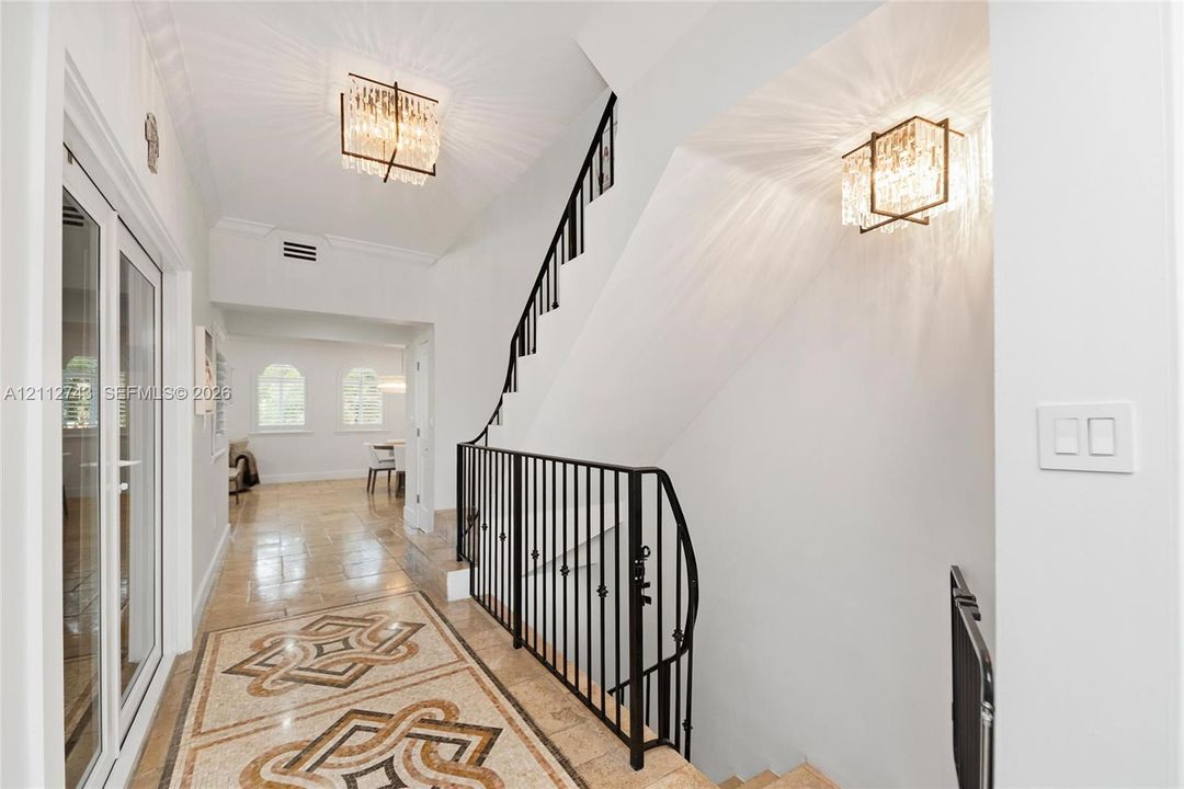 Foyer featuring intricate stone inlay flooring, black wrought-iron staircase railing, and tiered crystal flush-mount lighting