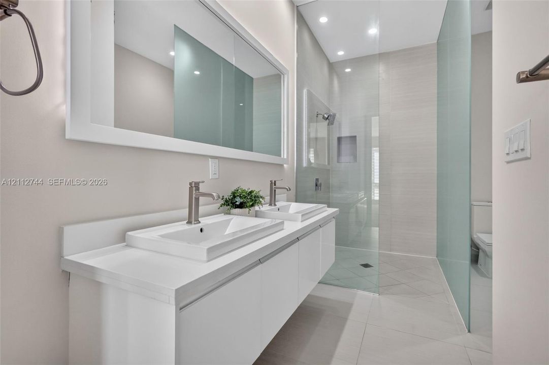 Double floating vanity with rectangular sinks, integrated mirror, glass-enclosed shower featuring a recessed niche, and stone-finish floor tiling