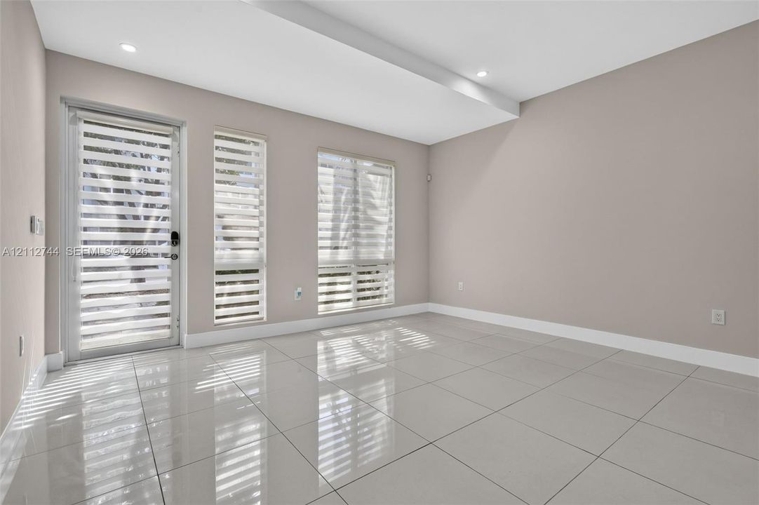 Neutral-toned interior featuring large-format polished tile flooring, recessed ceiling lighting, a glass-panel exterior door, and multiple windows with adjustable roller shades