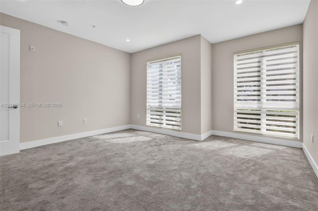 Neutral-toned interior featuring wall-to-wall carpeting, recessed ceiling lighting, and two windows equipped with dual-layer zebra shades