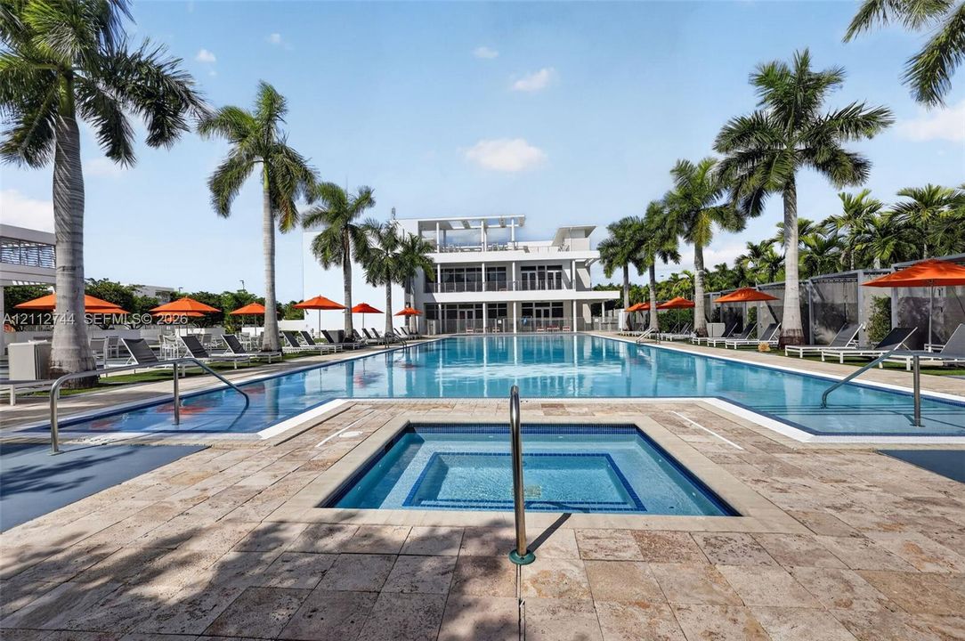 Large swimming pool featuring a built-in spa, stone paver decking, and mature palm trees