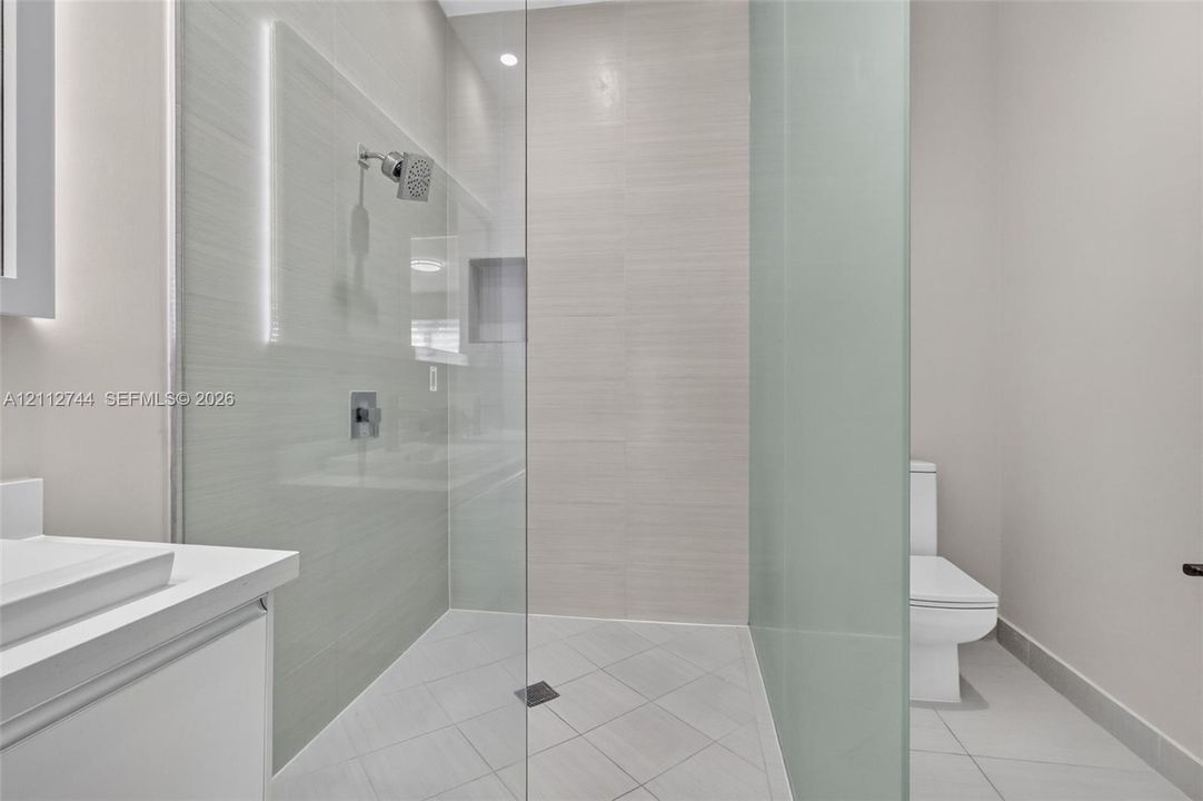 Walk-in shower featuring glass enclosure, wall-mounted shower head, recessed shelving, and tiled flooring