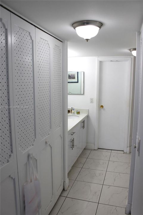 Floor-to-ceiling white cabinetry with textured detail, white vanity with rectangular under-mount sink, stone-finish tile flooring, and flush-mount lighting fixtures