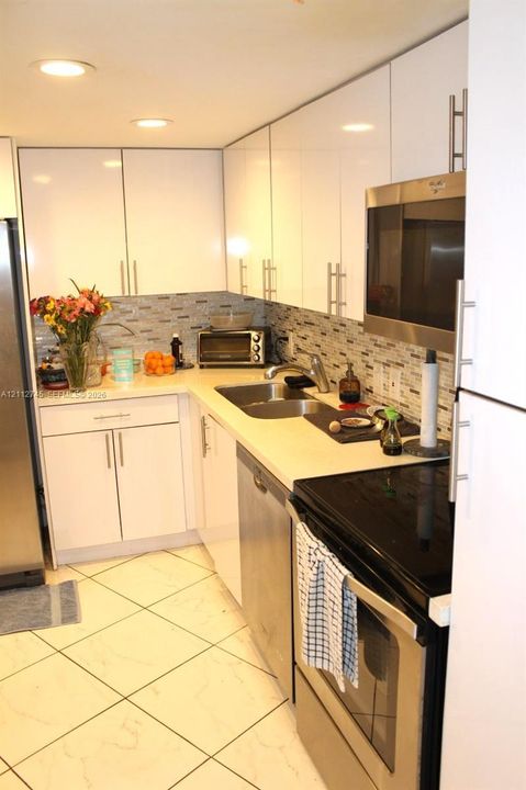 Kitchen featuring white high-gloss cabinetry, stainless steel appliances, tiled backsplash, solid surface countertops, and recessed lighting