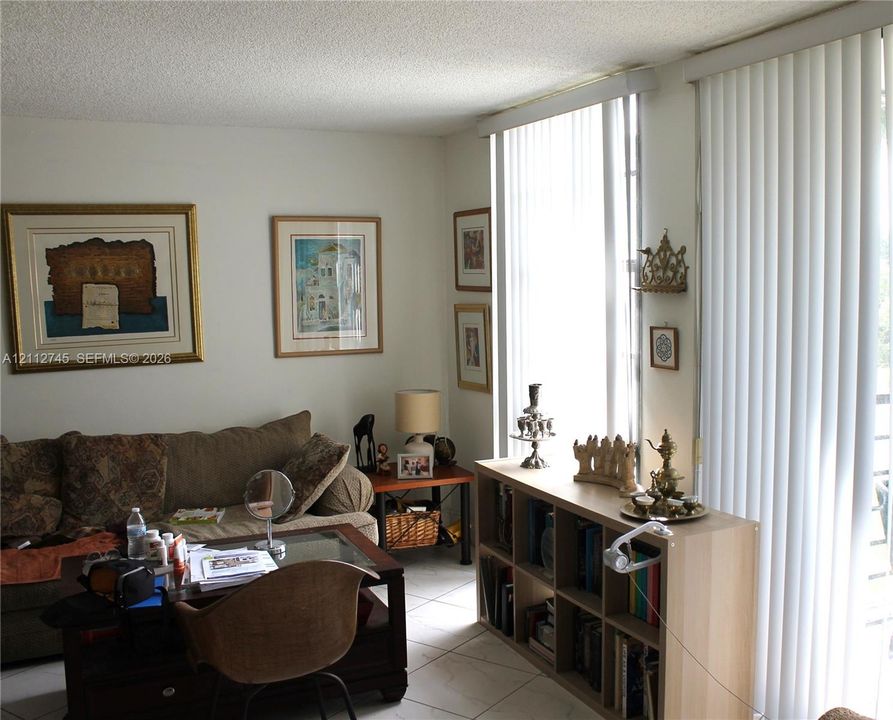 Living area featuring light-toned tile flooring, floor-to-ceiling windows, and vertical window treatments