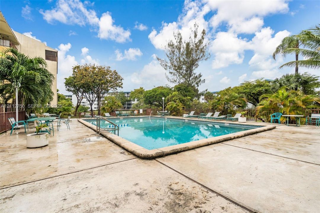 Swimming pool featuring a concrete deck, built-in metal entry handrail, and mature landscaping