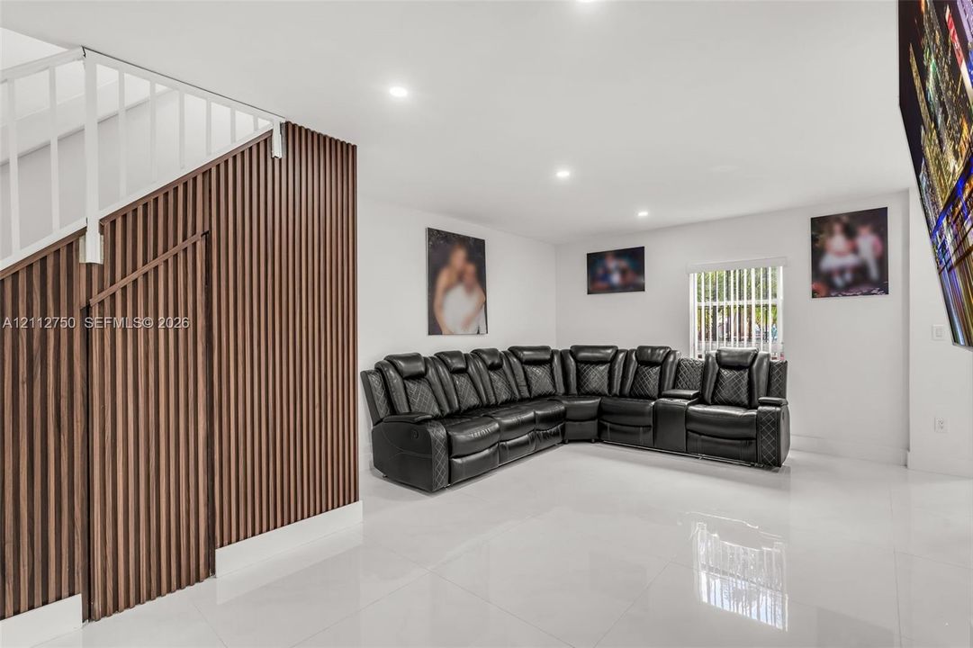 Living area featuring large-format tile flooring, recessed lighting, and a floor-to-ceiling wood-slat accent wall with integrated staircase railing