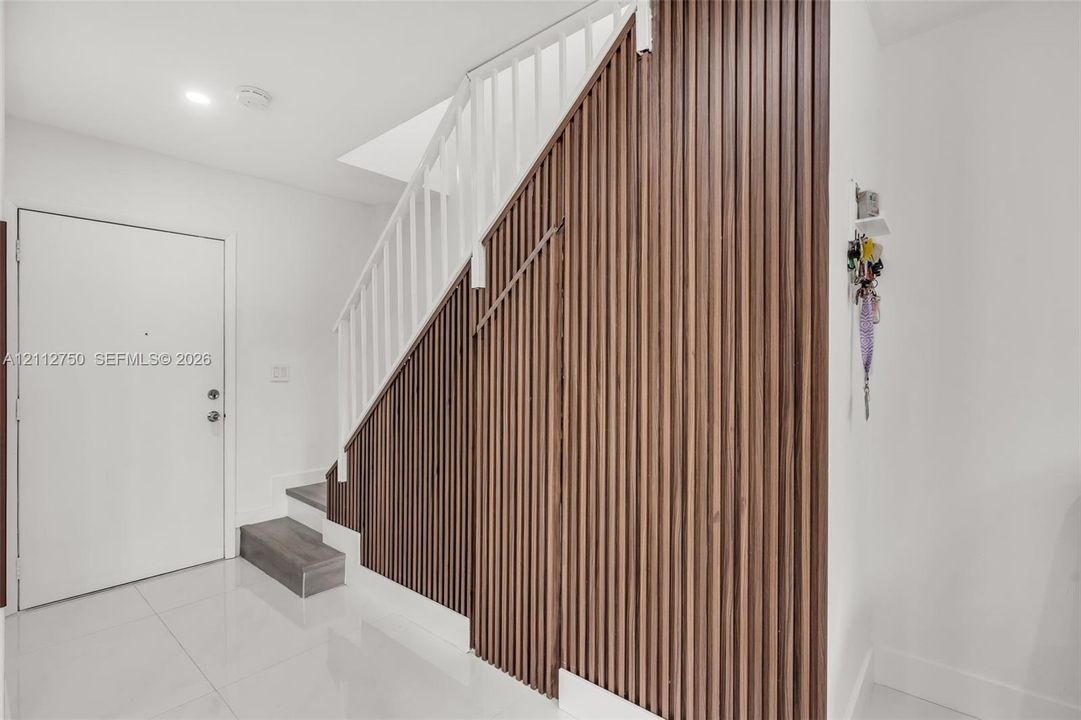 Entryway featuring vertical wood-slat wall paneling, white stair railings, polished tile flooring, and integrated under-stair cabinetry