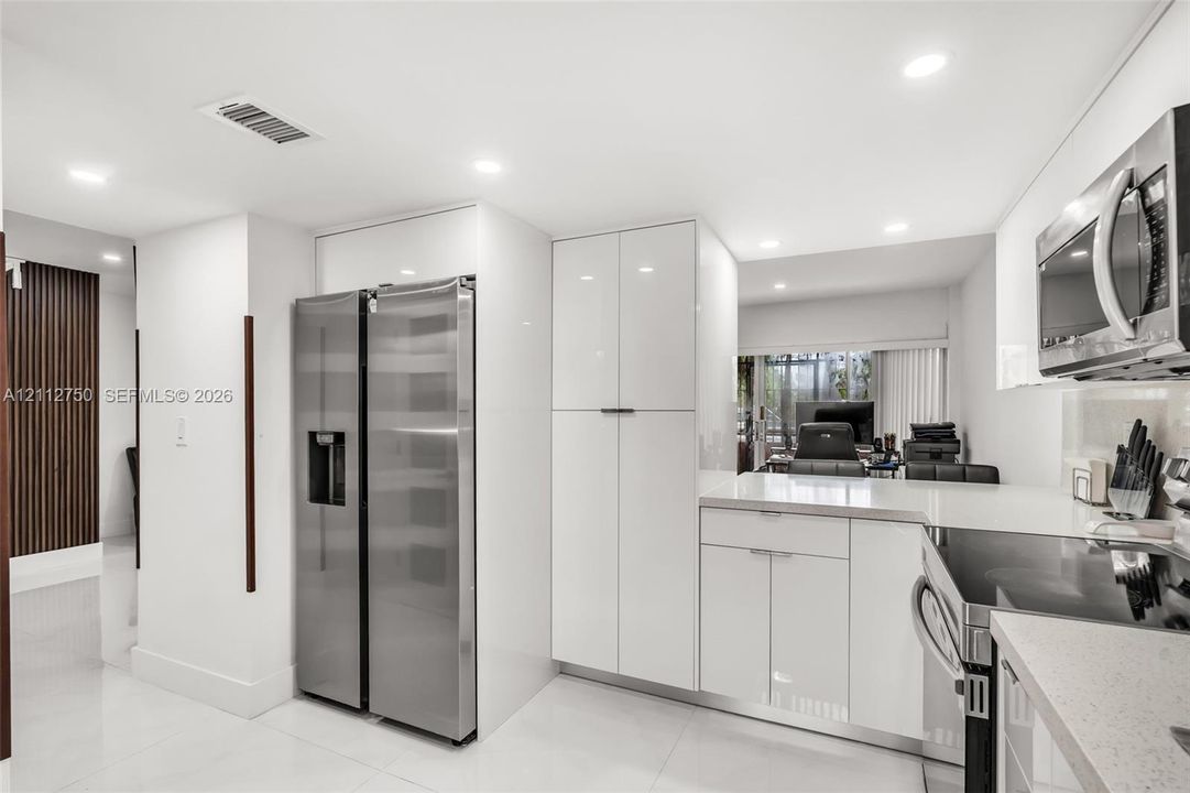 Kitchen featuring high-gloss white cabinetry, stainless steel appliances, quartz countertops, recessed lighting, and large-format tile flooring