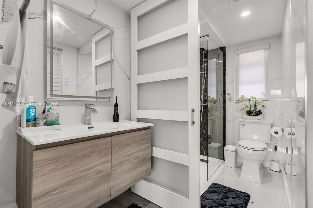 Floating wood-finish vanity with an integrated countertop, framed mirror, sliding glass panel door, and glass-enclosed shower featuring tiled surround
