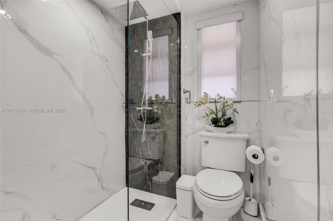 Walk-in shower enclosure with large-format wall tiling, rain-style showerhead, hand-held sprayer, and dark-toned decorative accent wall
