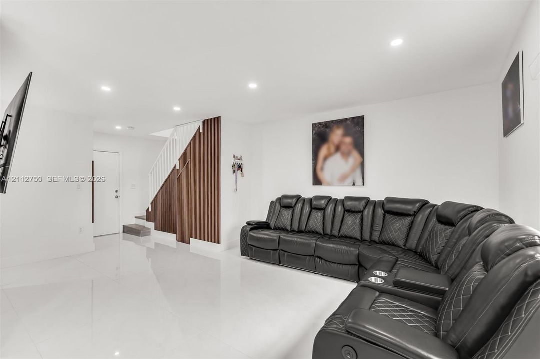 Open-concept interior featuring high-gloss tile flooring, recessed ceiling lighting, and a wood-slat accent wall with integrated staircase railing