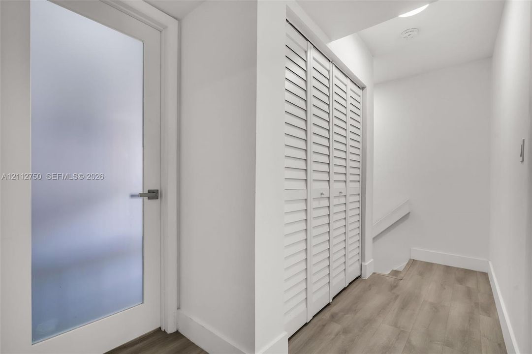 Frosted glass panel door with matte finish hardware, white louvered bifold closet doors, and wood-finish flooring