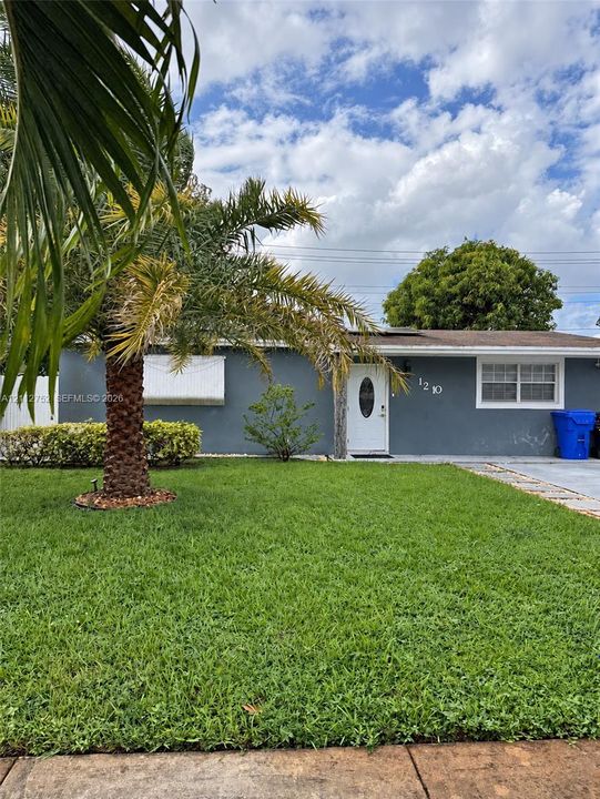 Single-story exterior featuring a gray stucco facade, white entry door with oval glass insert, multi-pane windows, and a mature palm tree on the front lawn