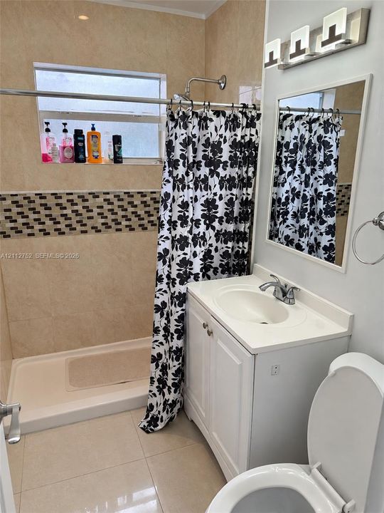 Full bathroom featuring tile wall finishes with mosaic accent inlay, a glass-enclosed shower, a white vanity with integrated basin, and modern multi-light fixture