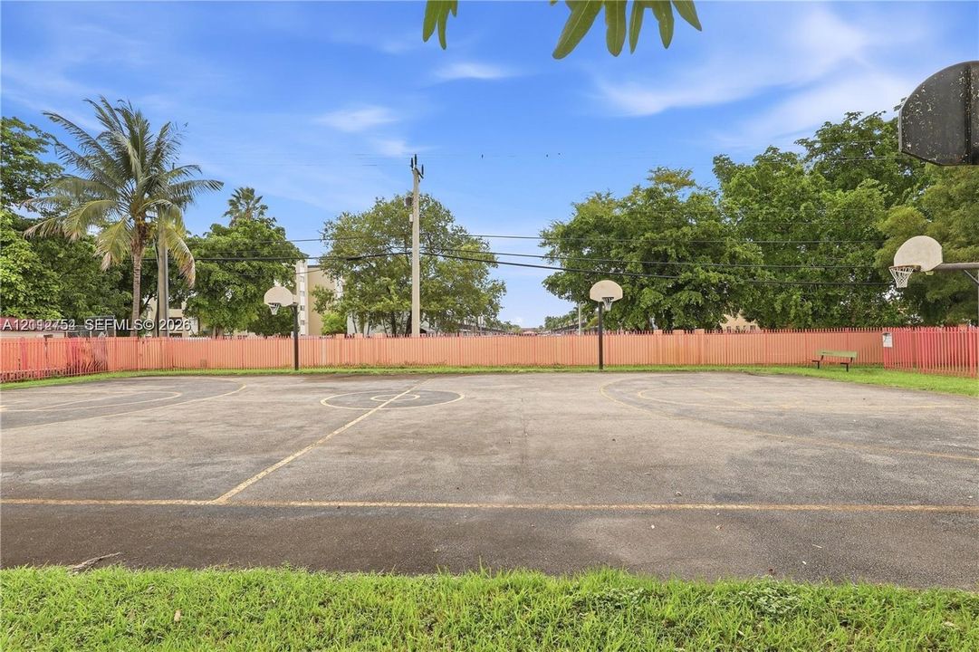 Outdoor basketball court featuring dual hoop systems, paved surface, and perimeter fencing