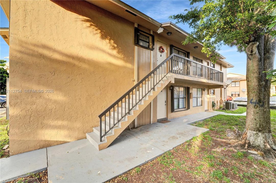 Stucco exterior featuring an elevated concrete staircase with a metal railing and a second-level balcony with metal balusters