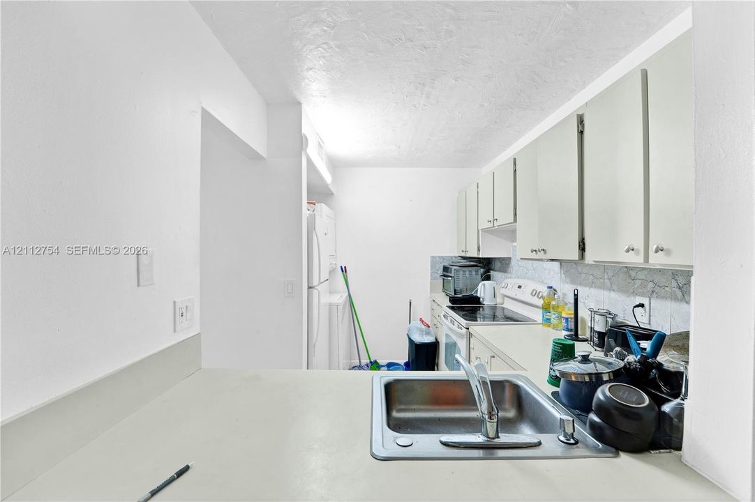 Kitchen featuring white cabinetry, solid-surface countertops, a stainless steel undermount sink, and a tiled backsplash