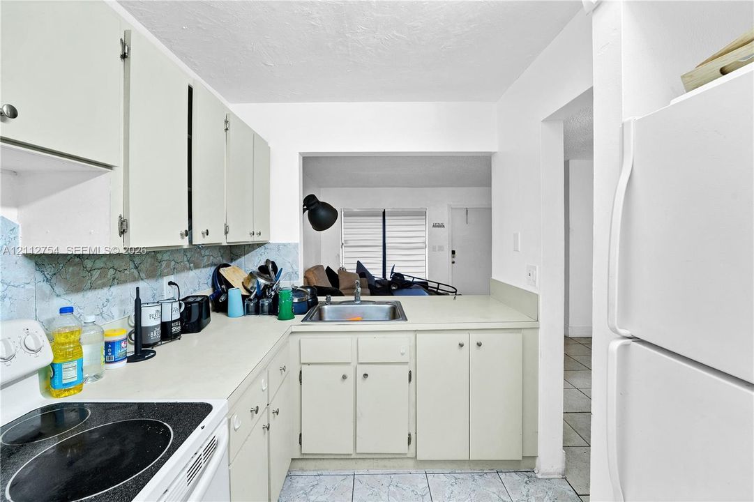Kitchen featuring solid-surface countertops, cabinetry with exposed hinges, a stainless steel sink, and tile flooring