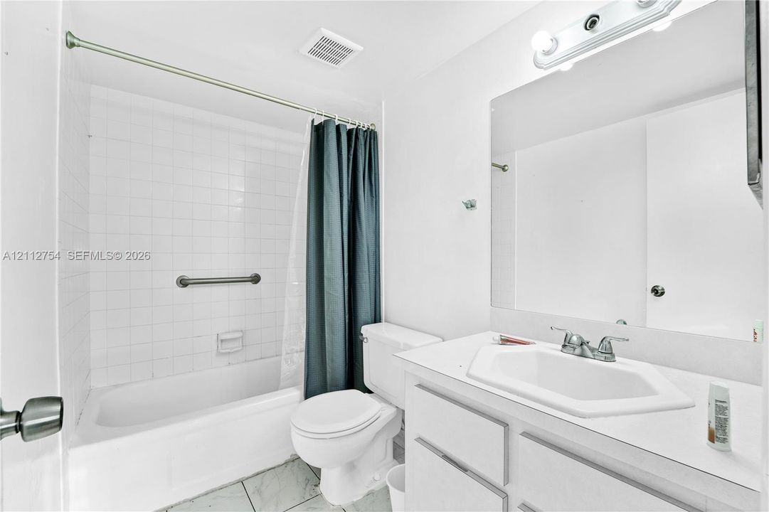 Bathroom featuring a vanity with a white countertop and integrated sink, a full-width wall mirror, a combination tub and shower with white tile surround, and neutral floor tiling