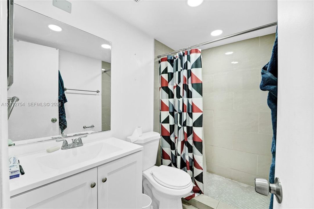 Bathroom featuring a white vanity with an integrated sink, polished chrome faucet, large wall-mounted mirror, and a walk-in shower with neutral tile surround and recessed lighting