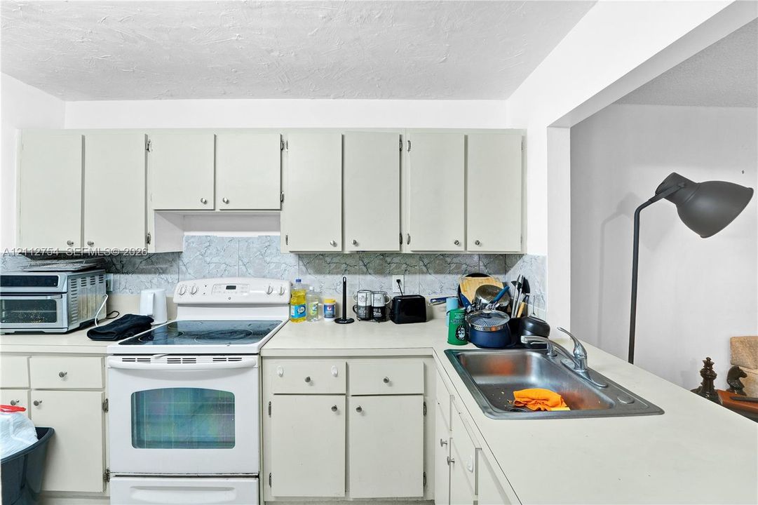 Kitchen featuring light-toned cabinetry, solid surface countertops, a white electric range, and a stainless steel sink with a chrome faucet