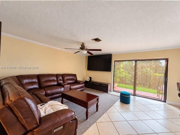 Spacious room featuring neutral wall paint, large-format tile flooring, a multi-blade ceiling fan, and sliding glass doors providing outdoor access