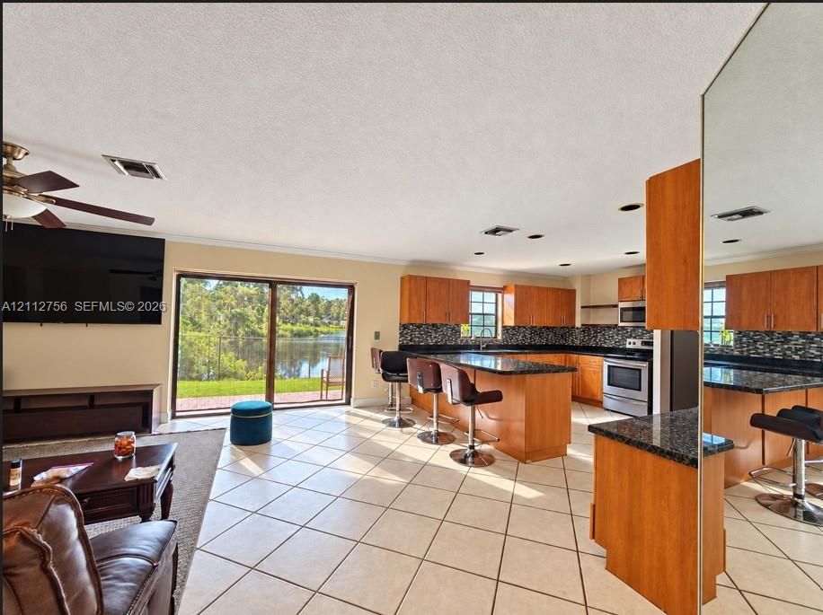 Open-concept kitchen featuring wood cabinetry, stone countertops, mosaic tile backsplash, stainless steel appliances, and tile flooring