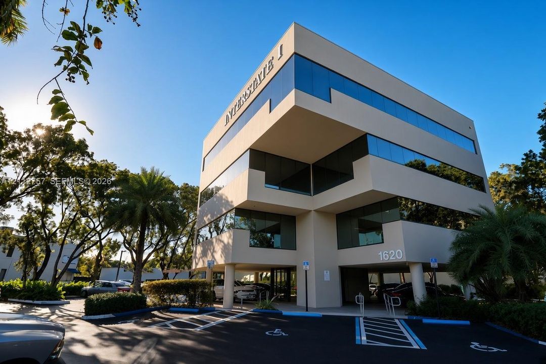 Three-story office building featuring a concrete exterior, tiered window design, covered ground-level parking, and paved surface lot
