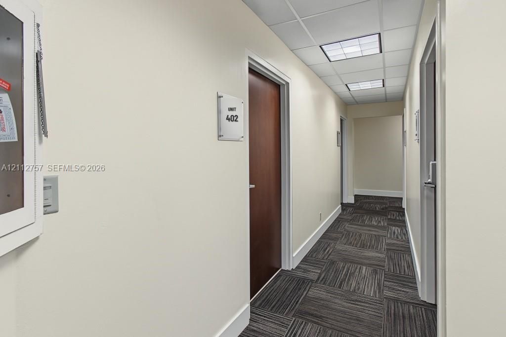 Hallway featuring patterned carpet tile flooring, recessed drop-ceiling lighting, and solid wood-finish doors