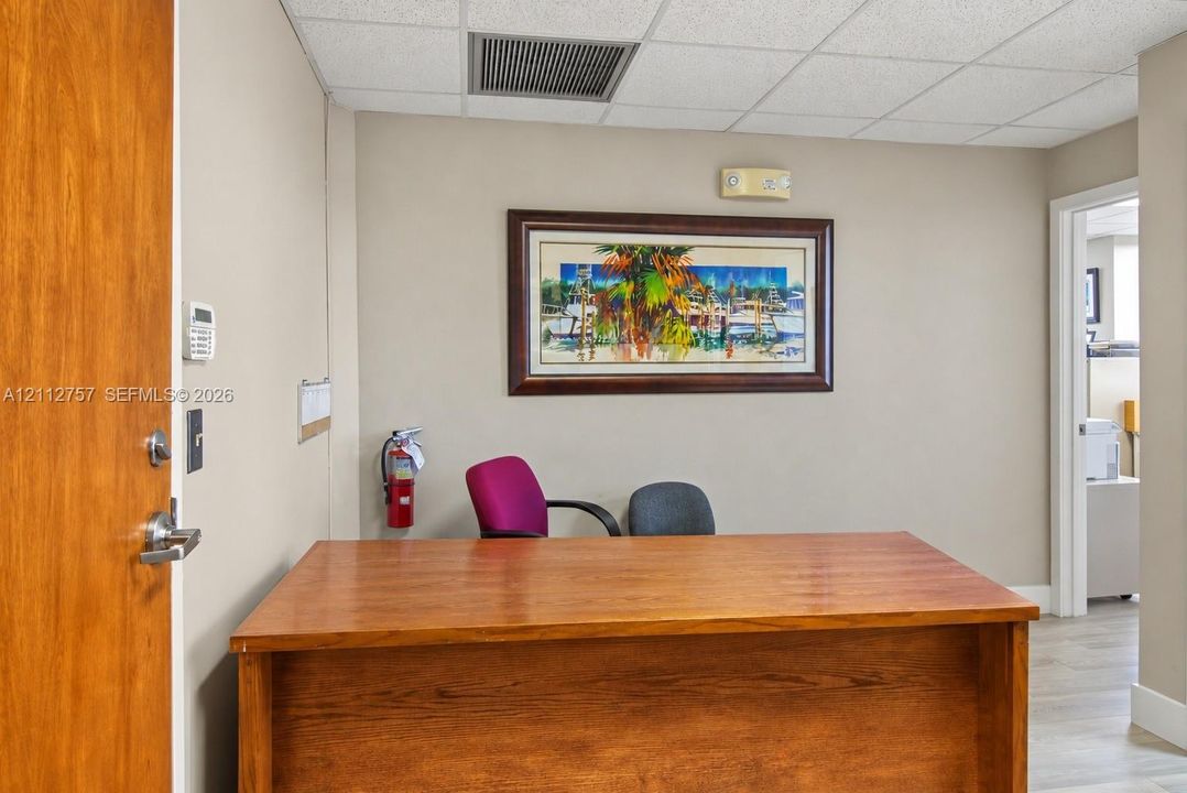Interior space featuring neutral wall tones, a drop ceiling, wood-finish door, and wood-finish desk