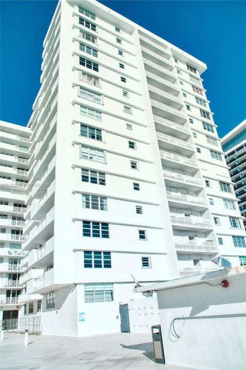 High-rise residential building featuring a white facade, multi-level private balconies, and grid-patterned windows