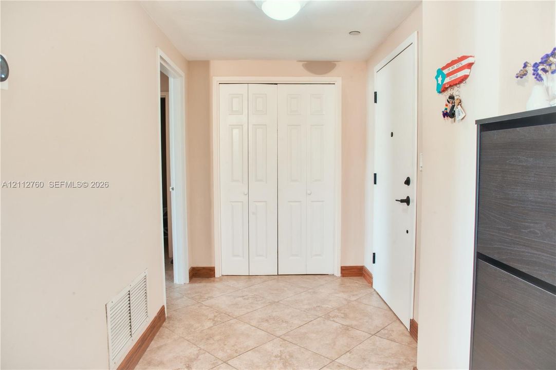 Entryway featuring tile flooring, white six-panel bi-fold closet doors, and a solid-core entry door with matte black hardware