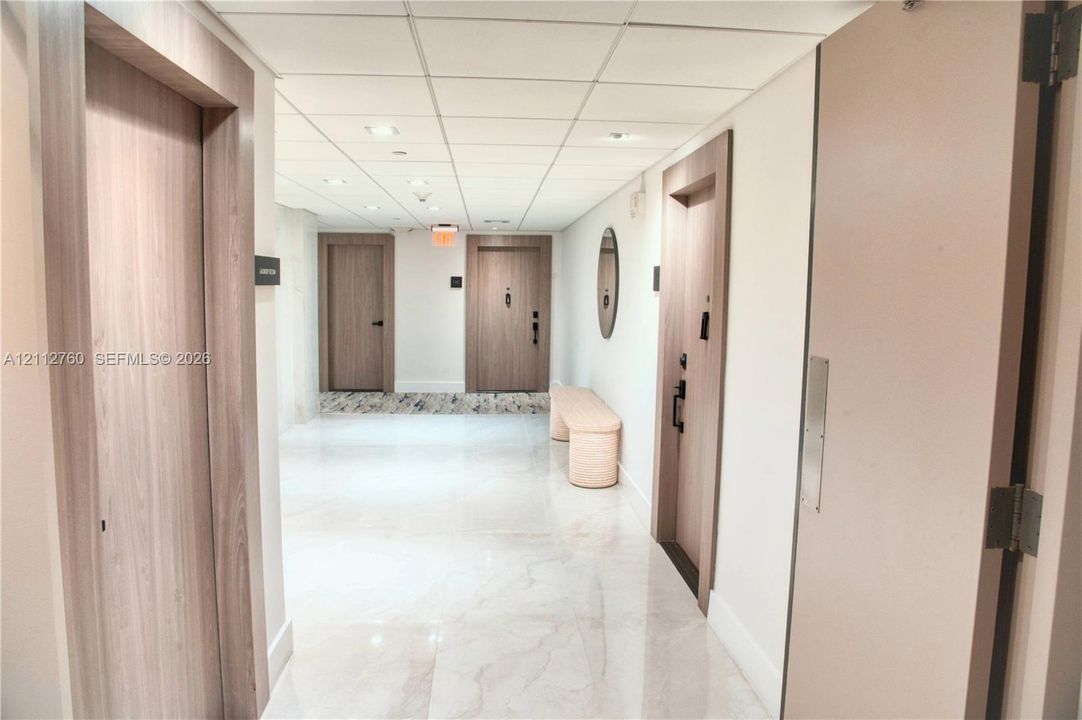 Interior hallway featuring polished stone-finish flooring, recessed ceiling lighting, and wood-finish door frames