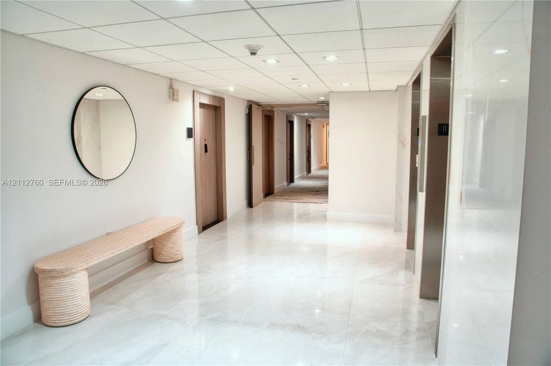 Common area hallway featuring polished stone-finish flooring, recessed ceiling lighting, and stainless steel elevator doors