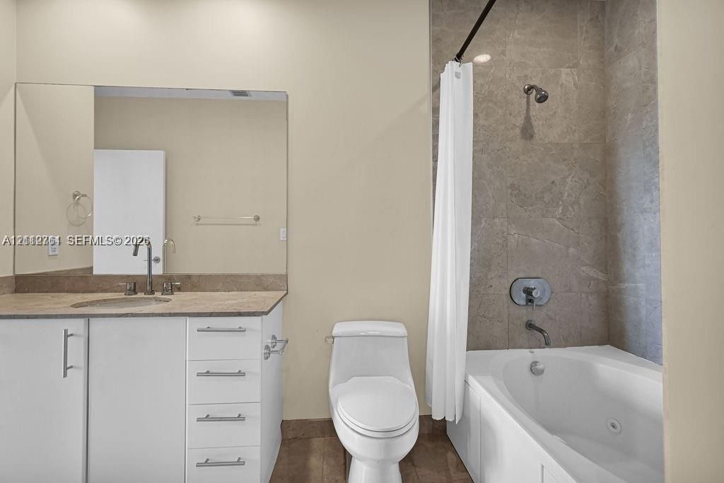 Bathroom featuring a white vanity cabinet with stone-surfaced countertop, integrated undermount sink, large wall-mounted mirror, and a tub with a stone-tiled surround and stainless steel fixtures