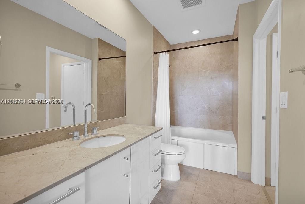 Bathroom featuring a full-width wall mirror, white cabinetry with a stone-surface countertop, an integrated oval sink, and a shower-tub combination with large-format tile surround
