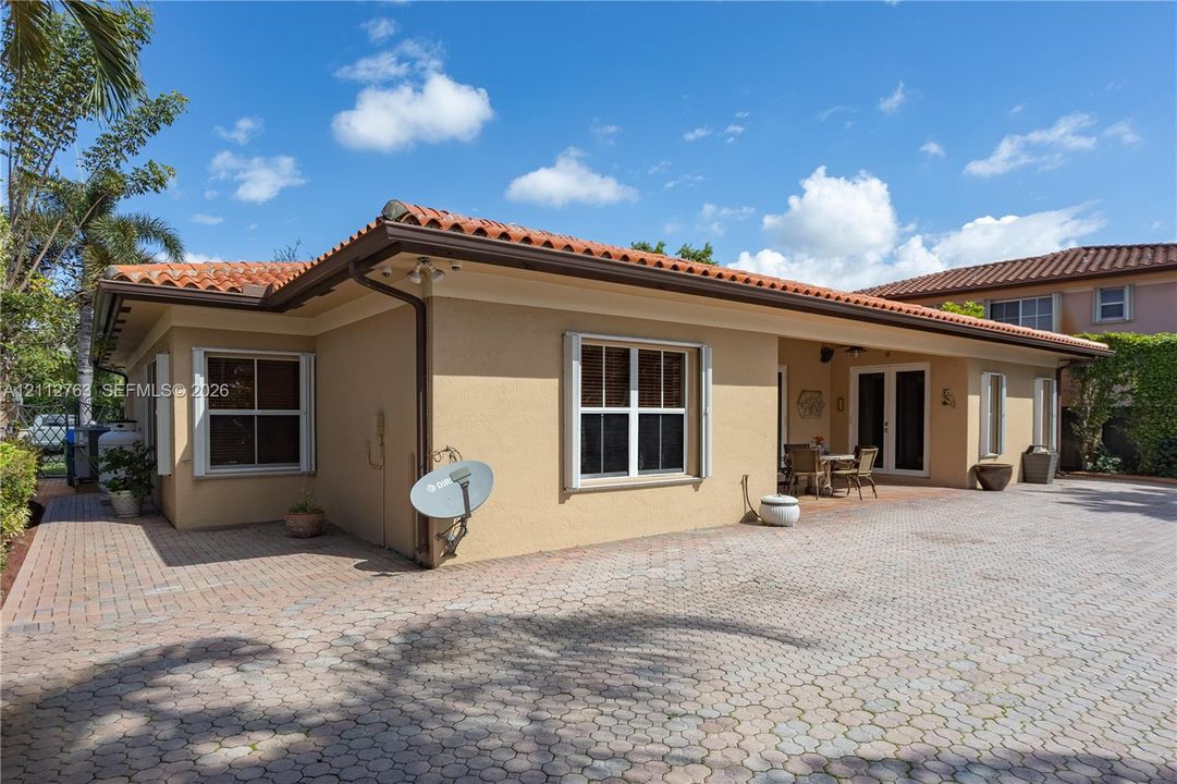 Stucco exterior featuring a clay tile roof, expansive brick-paver patio, and French-style doors