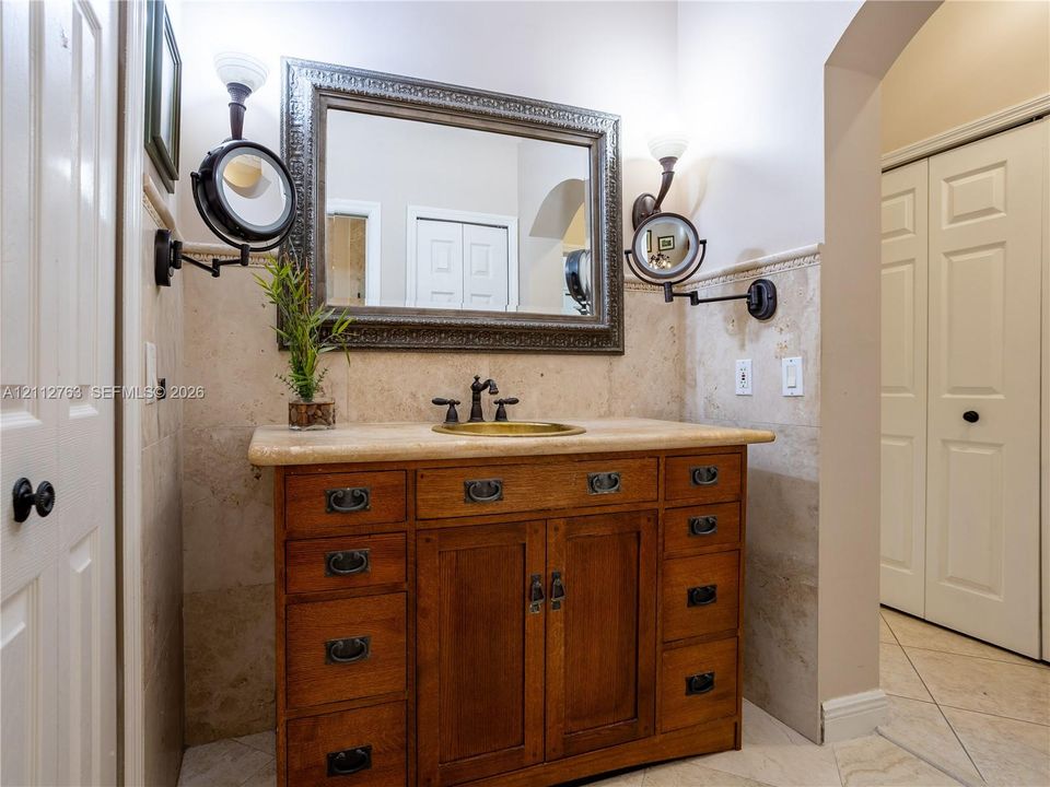 Custom wood vanity with multi-drawer storage, stone countertop, integrated vessel sink, wall-mounted swing-arm vanity mirrors, and stone-tiled wainscoting