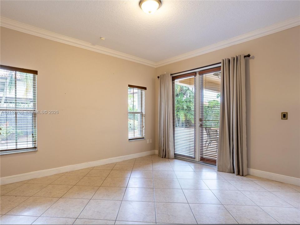 Neutral-toned interior featuring large-format tile flooring, crown molding, double glass-paneled exterior doors, and windows with integrated blinds