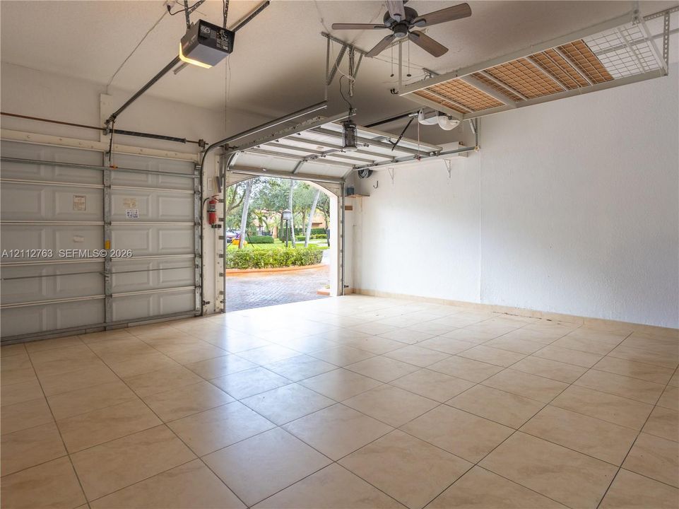 Multi-car garage featuring tile flooring, a ceiling-mounted storage rack, a motorized door opener, and a ceiling fan