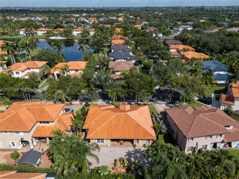 Aerial view featuring a terra cotta tiled roof, paved driveway, and mature palm trees within a residential landscape