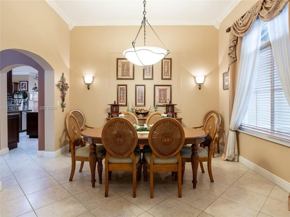 Formal dining area featuring high ceilings, neutral wall tones, tile flooring, crown molding, and a central pendant light fixture
