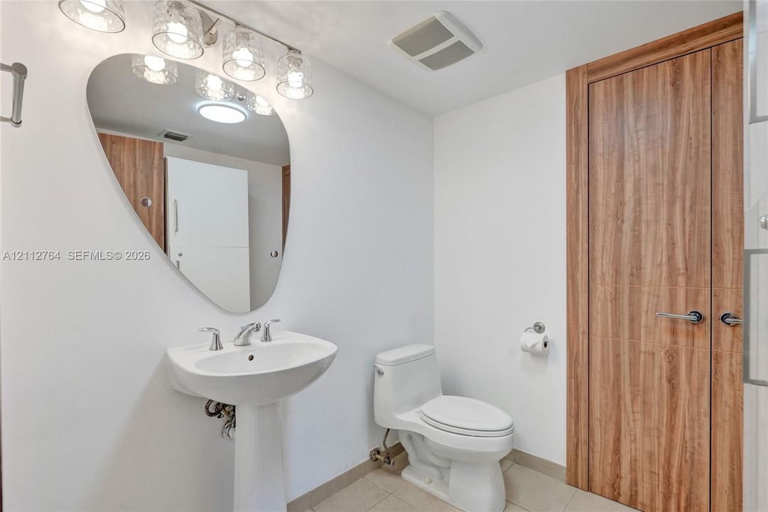 Pedestal sink featuring a curved mirror, wood-finish door, four-light vanity fixture, and tile flooring