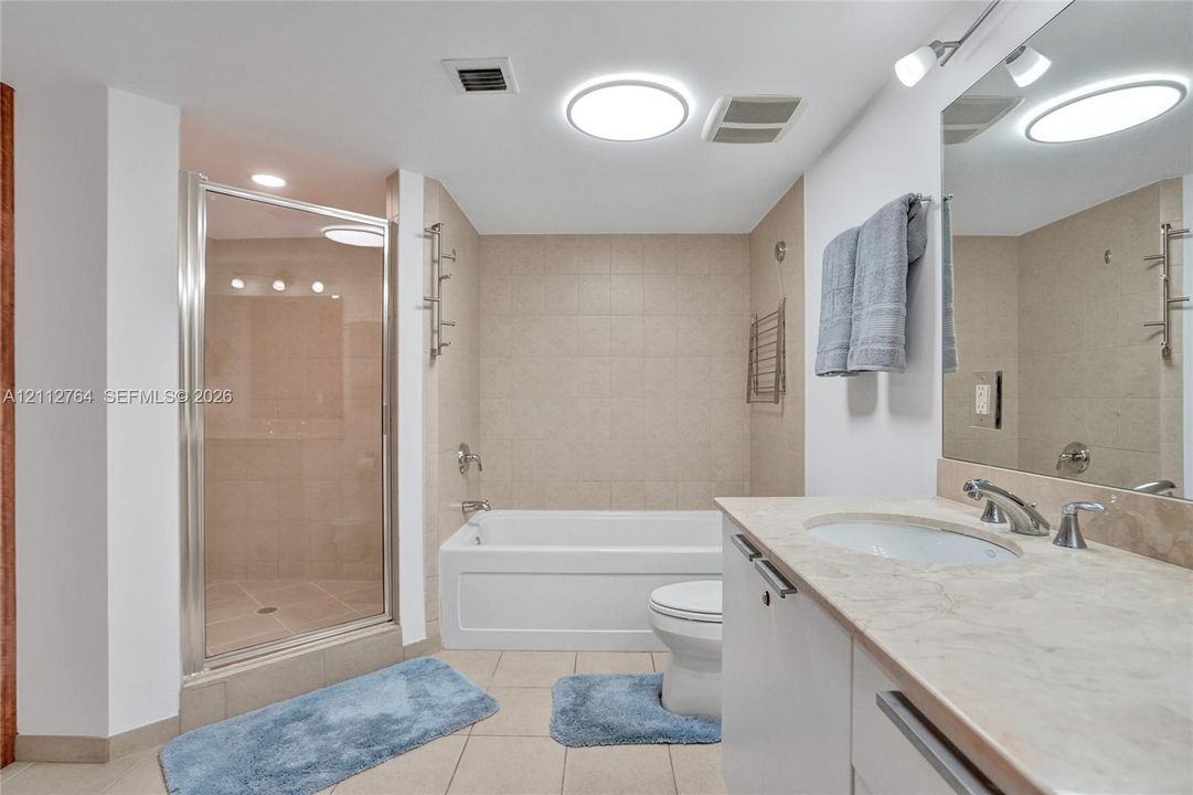 Bathroom featuring a glass-enclosed shower, deep soaking tub, tile surround, stone-composite vanity countertop, and wall-mounted mirror