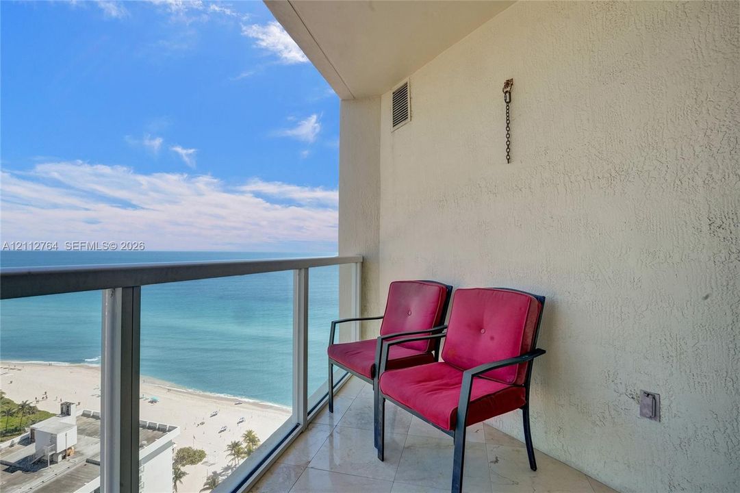 Covered balcony with stone-tile flooring and glass panel railing overlooking the oceanfront